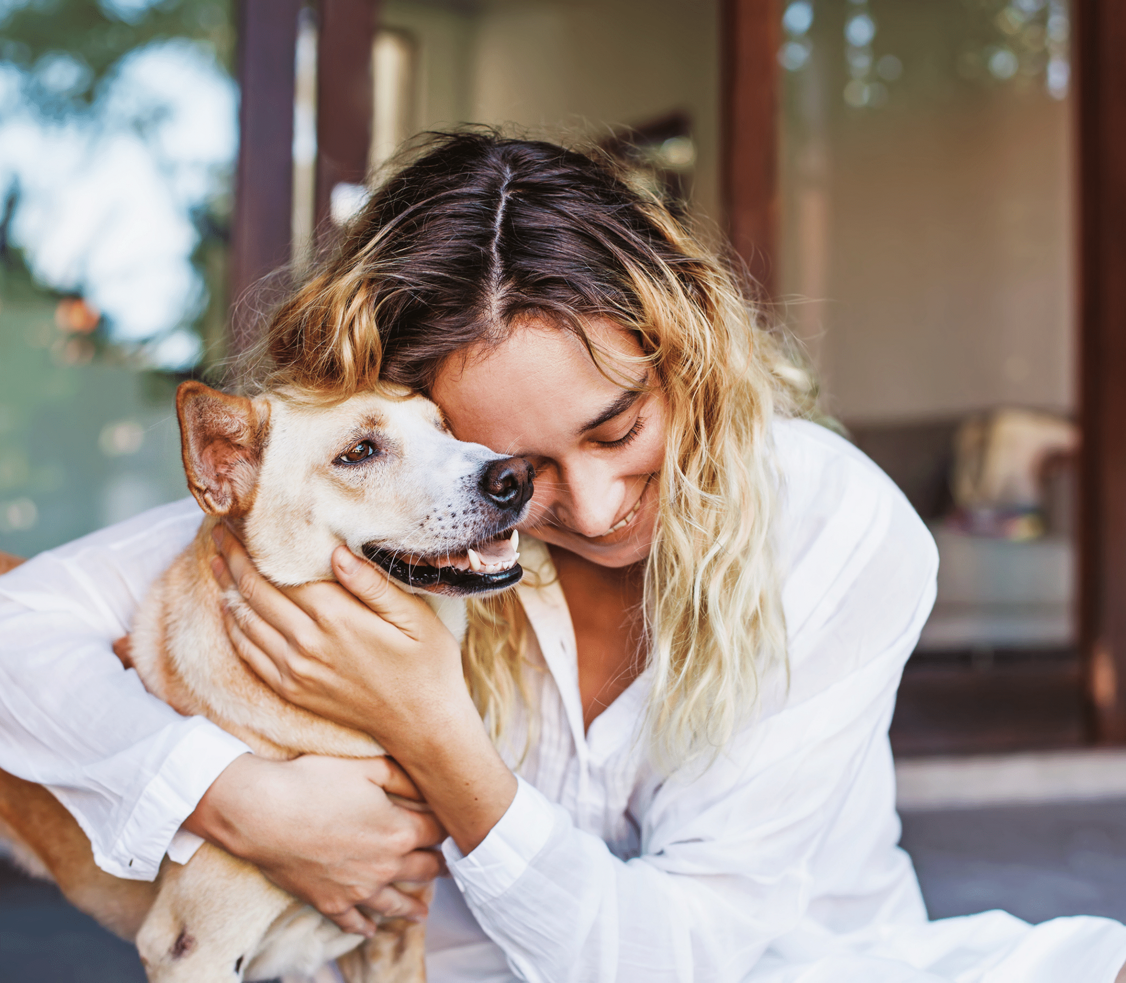 Lady in blonde hair and white long shirt hugging a dog
